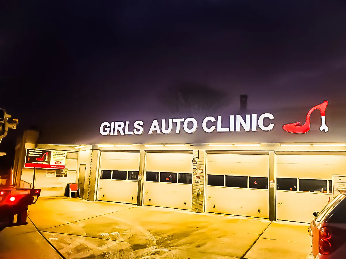 Girls Auto Clinic storefront at night with yellow lighting and high-heel logo