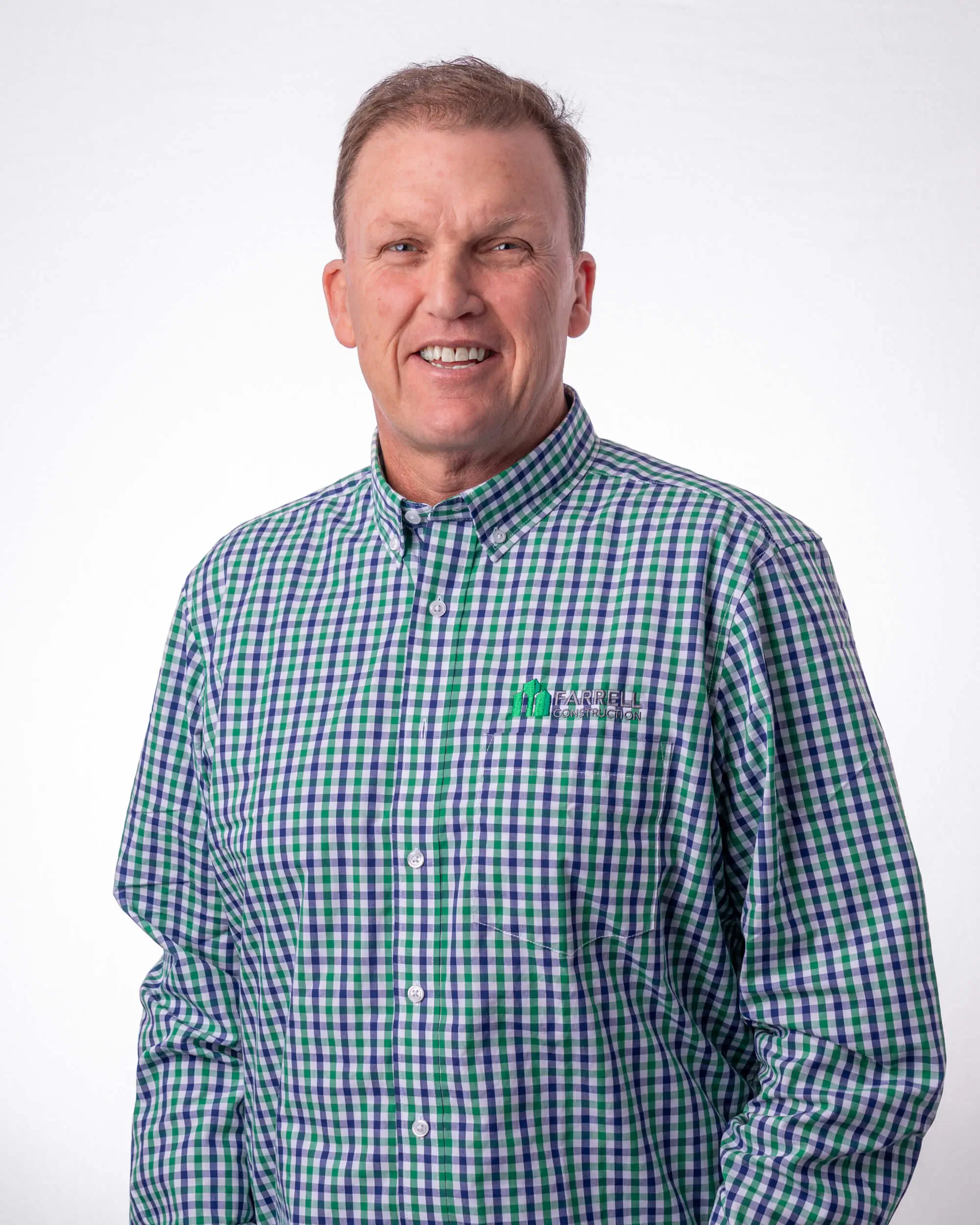 Sean Farrell the Owner and Director is a smiling middle-aged man wearing a green and blue checkered shirt with Farrell Construction logo.