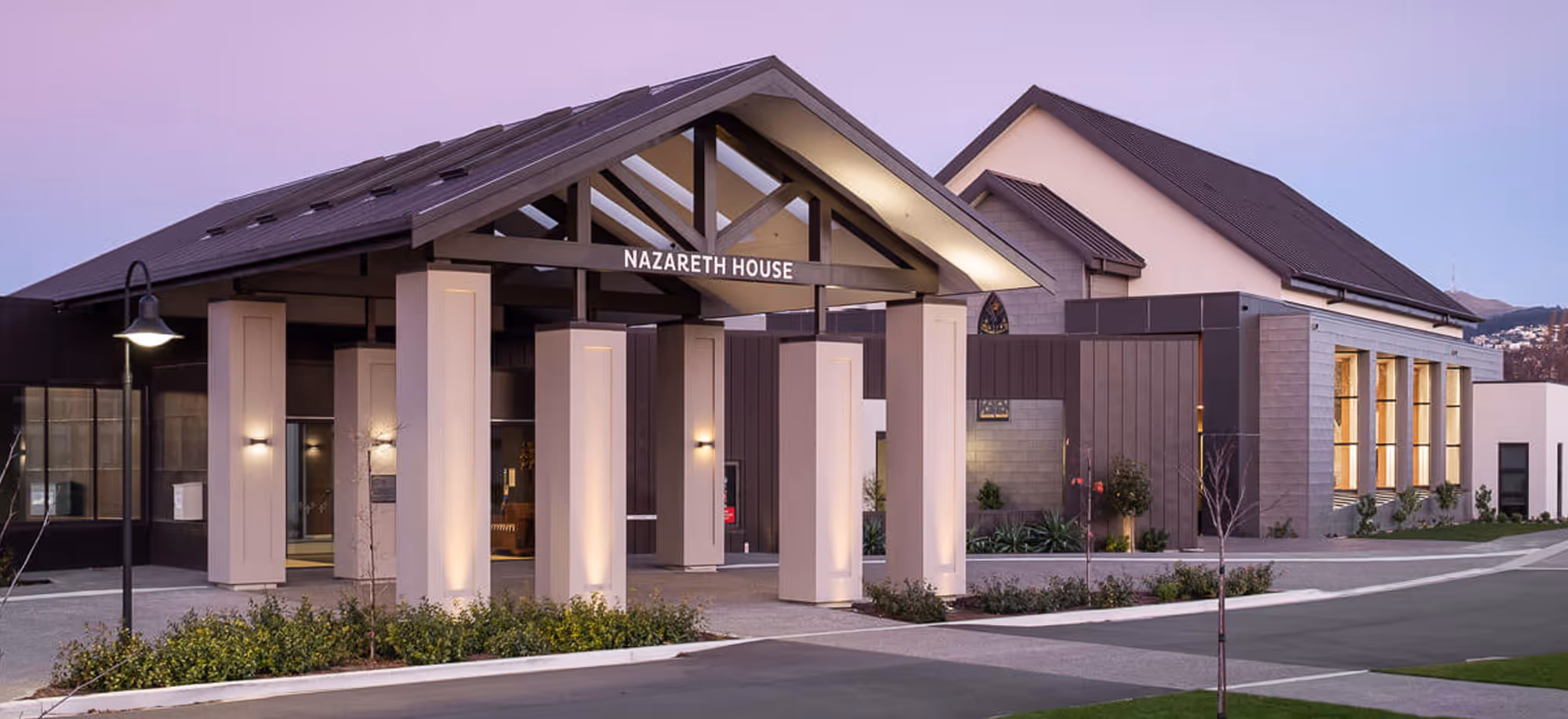 Modern building entrance with pillars and sign reading Nazareth House during dusk.