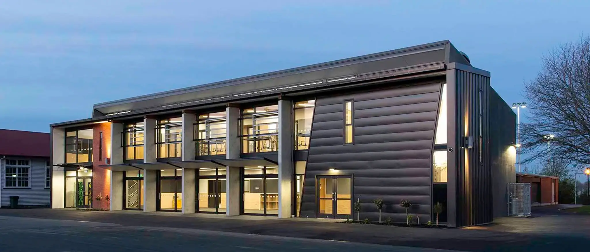 Modern two-story St Bedes School building with large windows and illuminated interior at dusk.