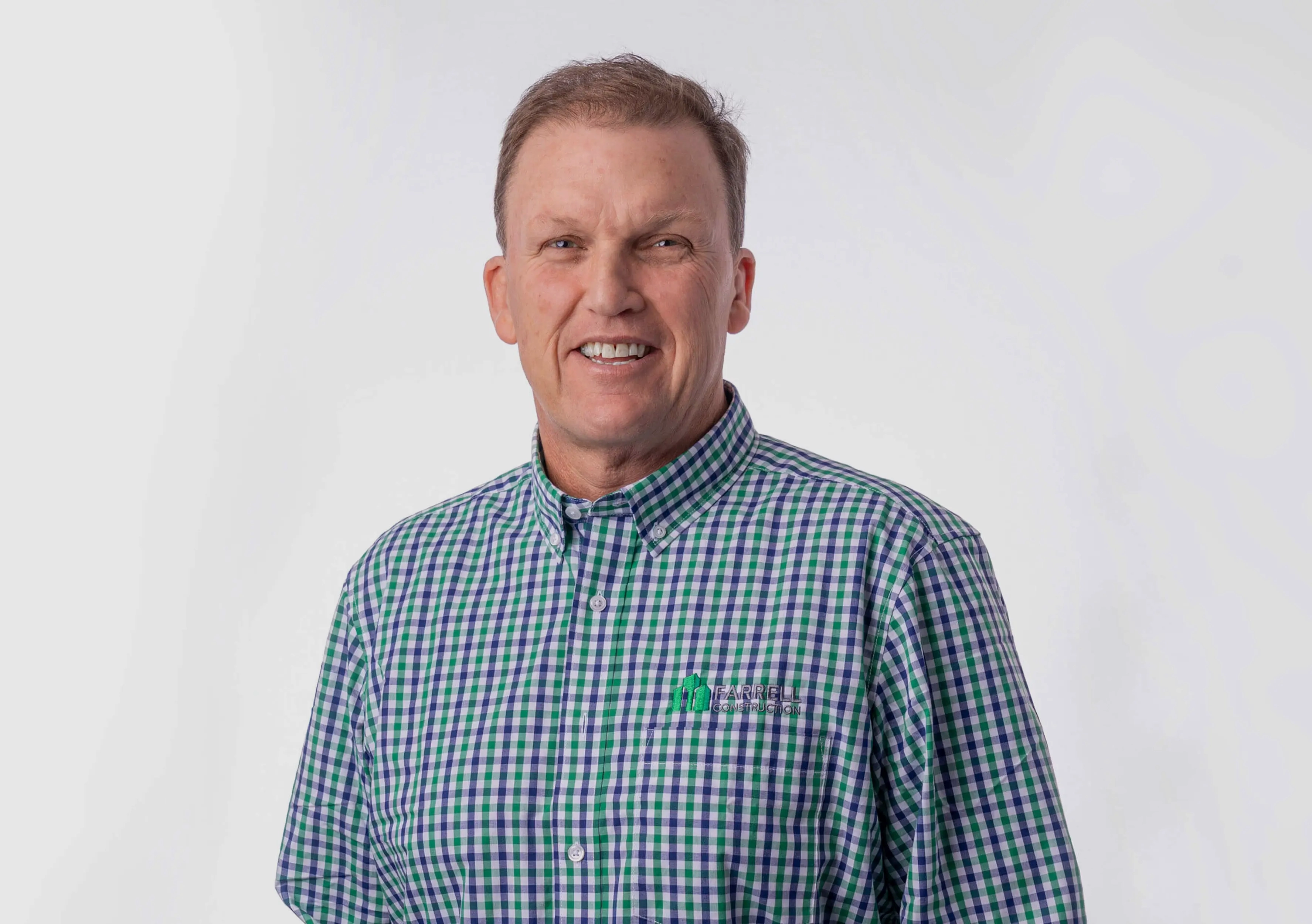 Smiling man Sean Farrell wearing a green and blue checkered shirt with Farrell Construction logo on pocket.