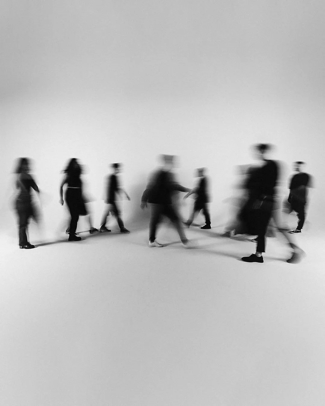Gruppe von Menschen in dunkler Kleidung geht aneinander vorbei, verschwommene Silhouetten vor weißem Hintergrund – abstrakter Eindruck von Bewegung