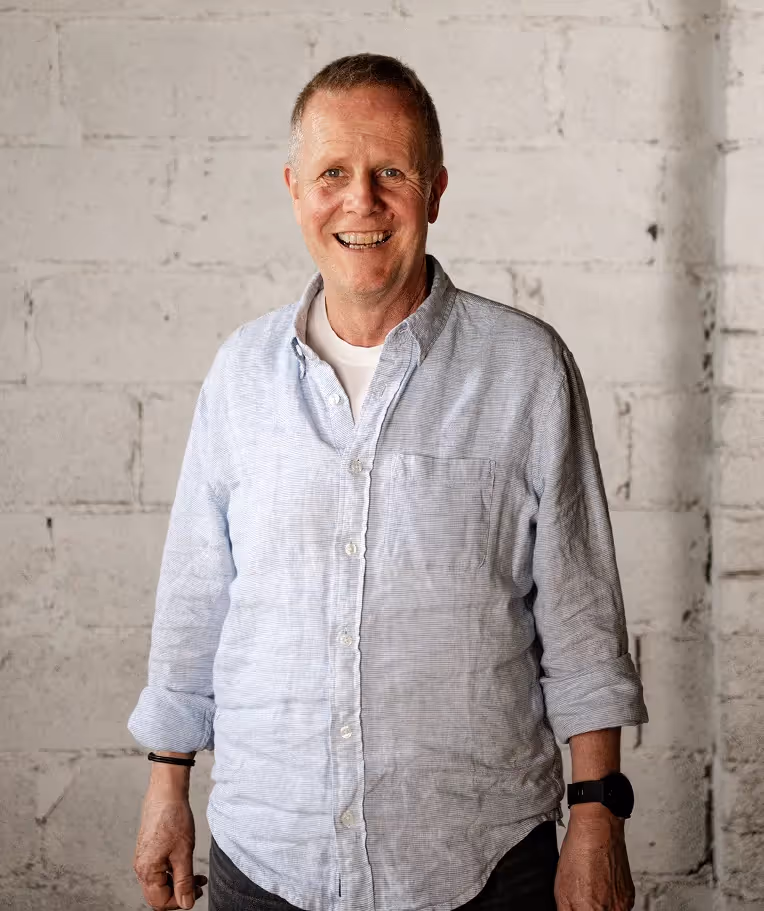 Klaus Metzger, HR-Experte und Autor, lächelt in hellblauem Hemd vor einer weißen Backsteinwand – Spezialist für strategische Positionierung von HR und Transformation in Unternehmen.