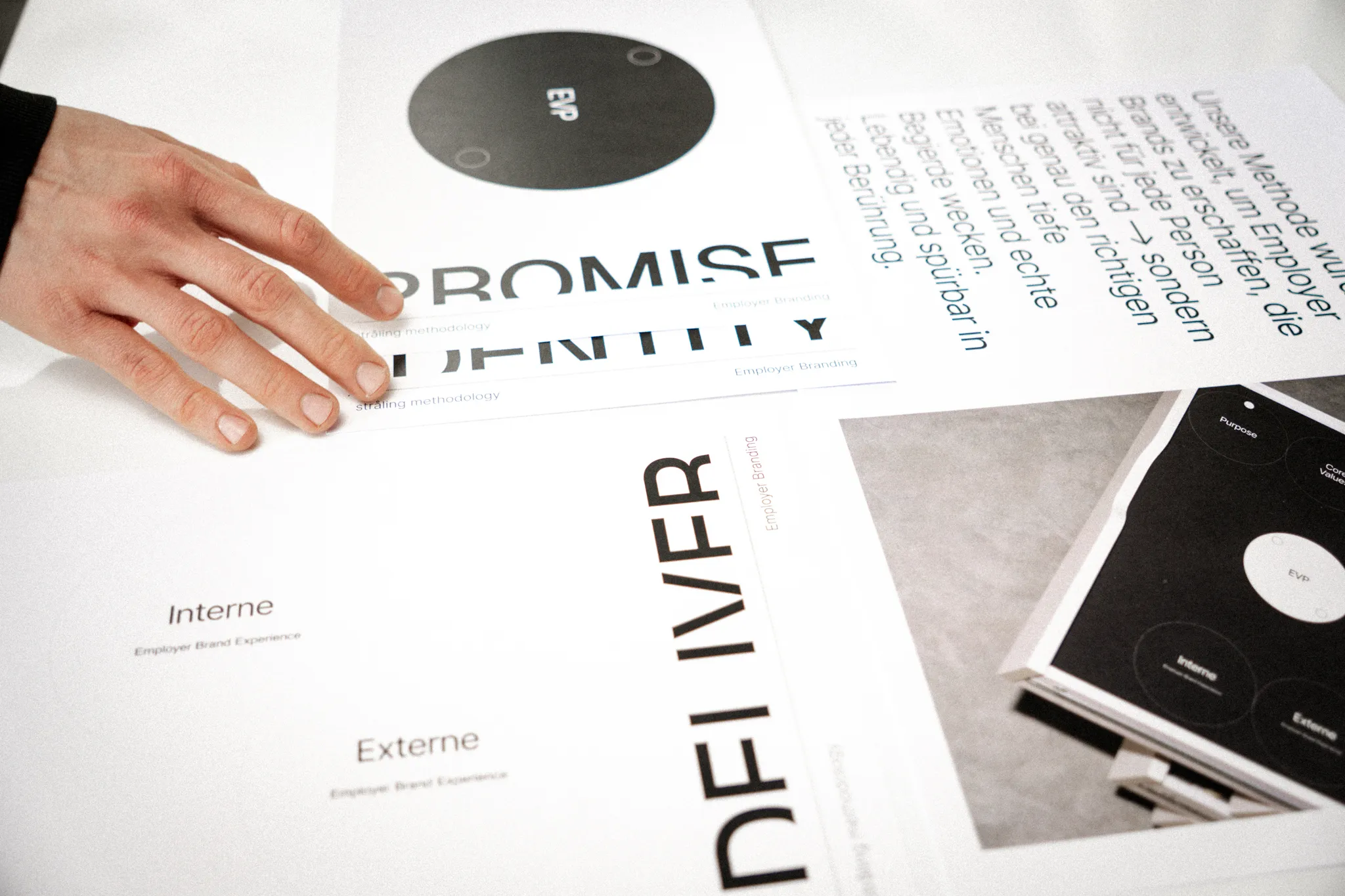 Hand legt Unterlagen mit Employer Branding Konzepten aus – Fokus auf EVP, Identität, interne und externe Brand Experience. Strategische Darstellung von Employer Branding Methoden einer spezialisierten Agentur