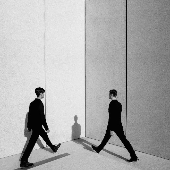 Effektives Assessment: zwei Personen treffen sich an einer Wandkante, klare Linien und Schatten – Symbol für strukturierte, objektive Bewertung.
