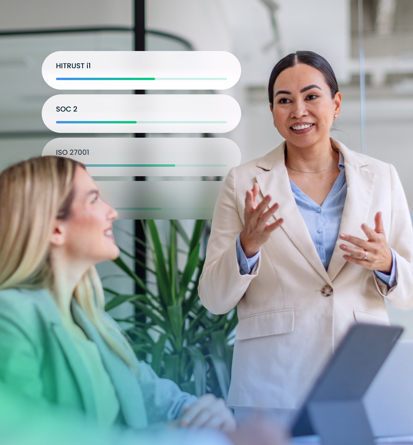Two professional women in an office setting engaged in a conversation, one standing and gesturing while the other listens seated with a laptop, with a semi-transparent overlay showing progress bars labeled HITRUST i1, SOC 2, and ISO 27001.