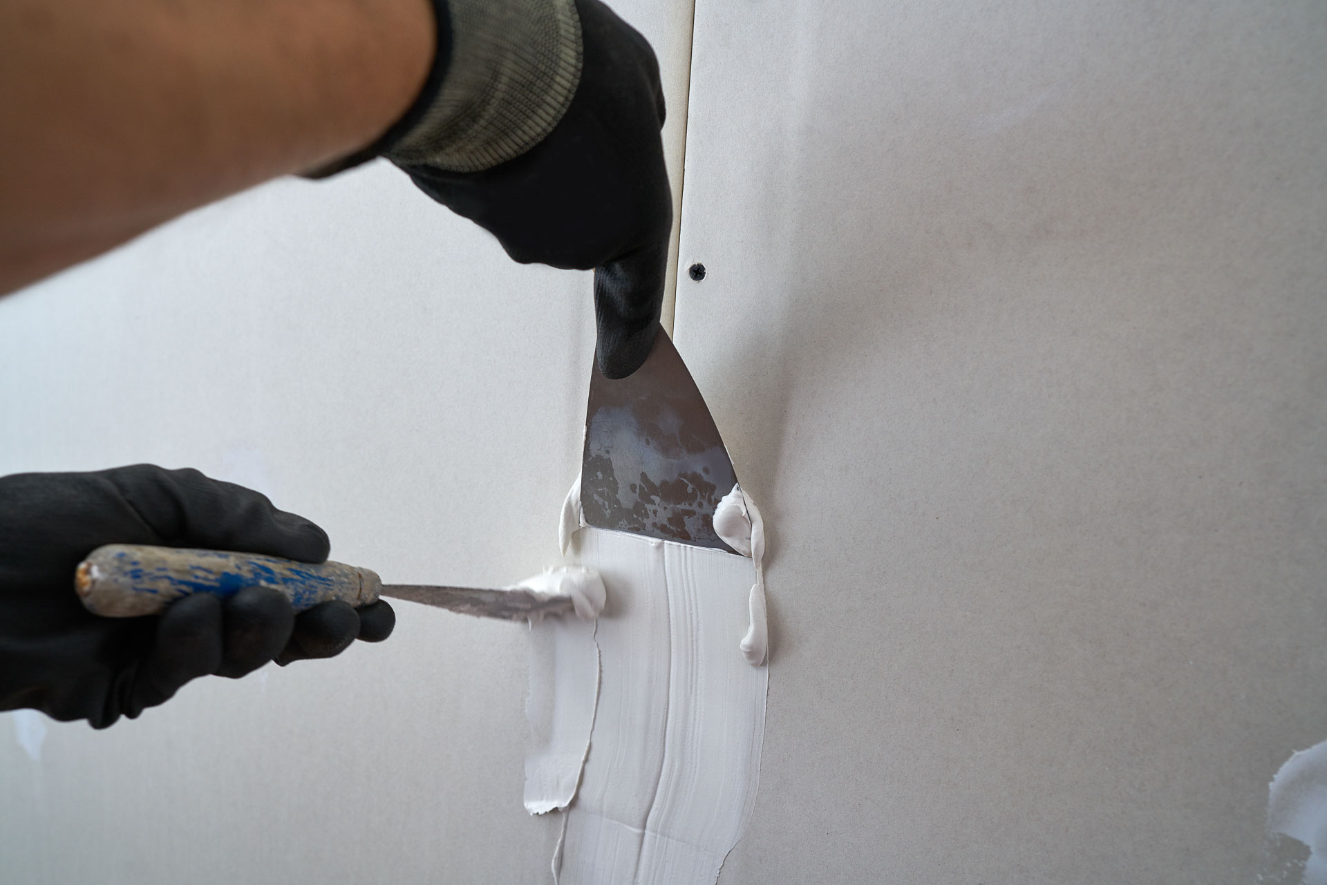 Applying drywall joint compound with a putty knife for wall repair.