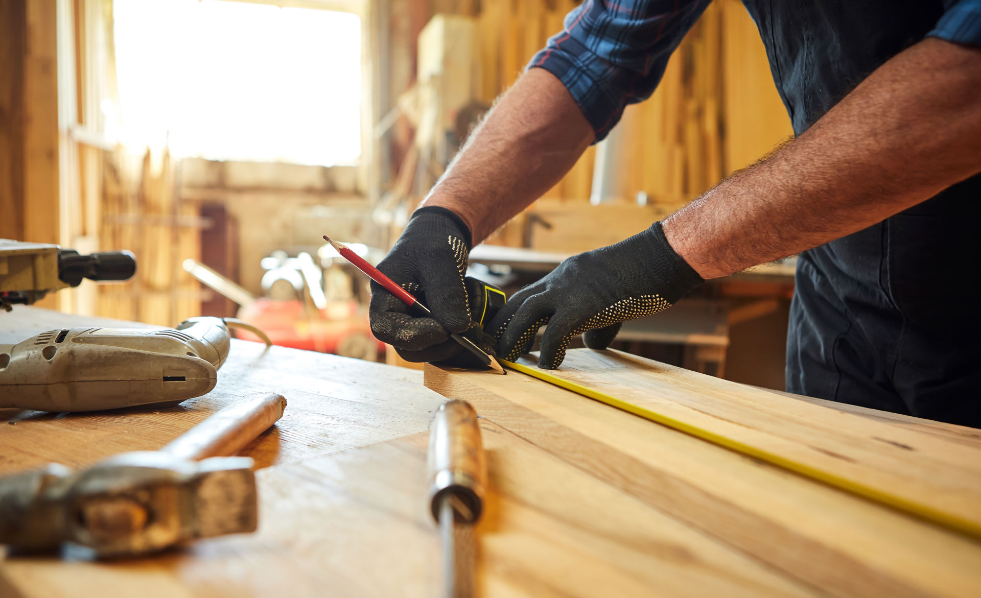 Woodworker measuring timber with tape measure and pencil in workshop.