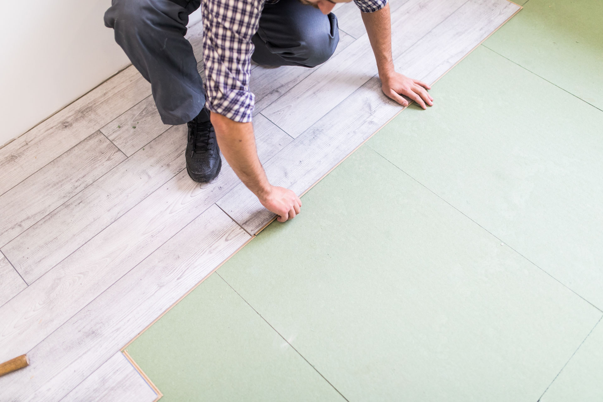Worker installing laminate flooring with underlayment in a residential space.