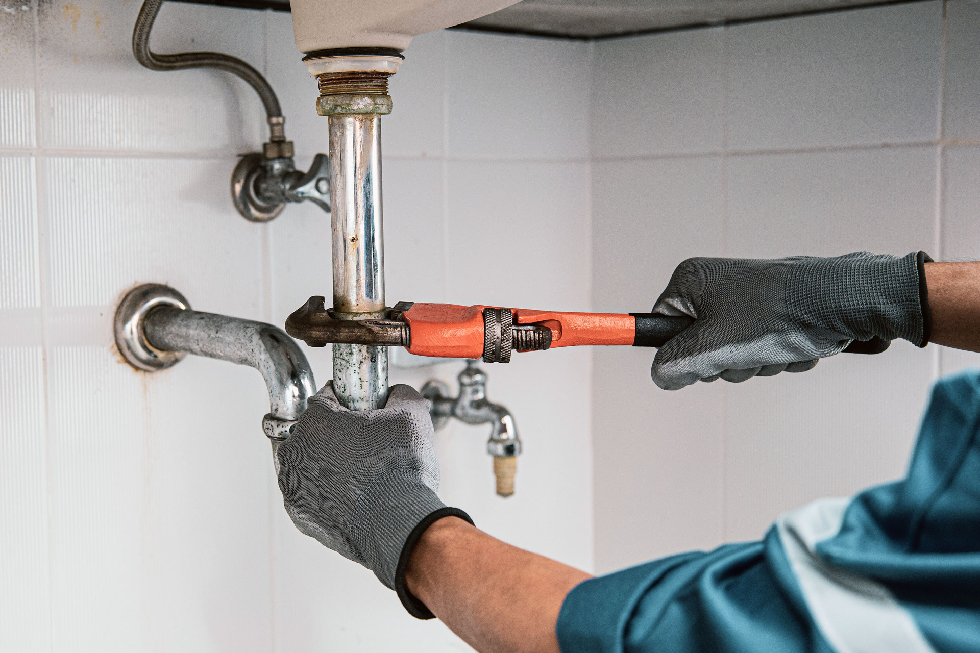 Plumber using wrench to fix sink pipe in kitchen.