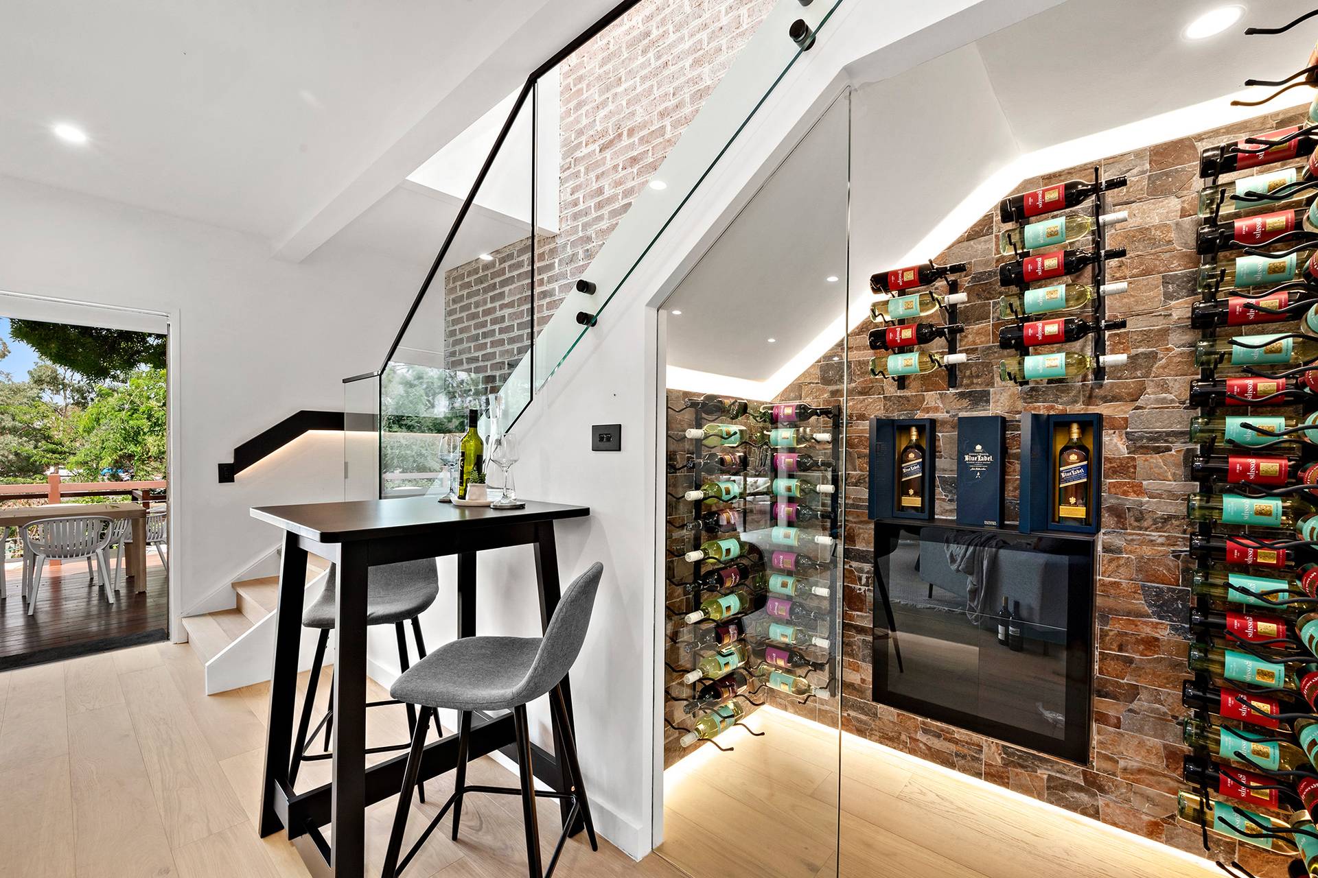 Modern home wine cellar under staircase with glass walls and minimalist design.