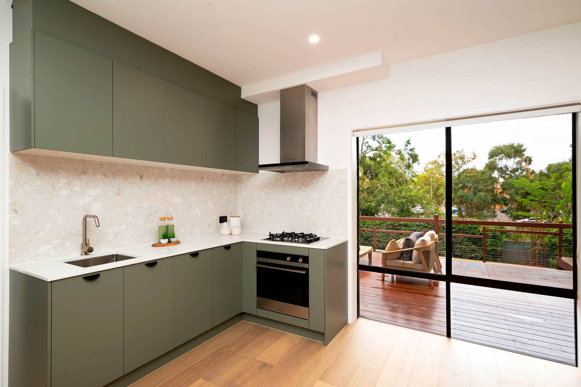 Modern kitchen with green cabinets, marble backsplash, and sliding glass doors to deck.