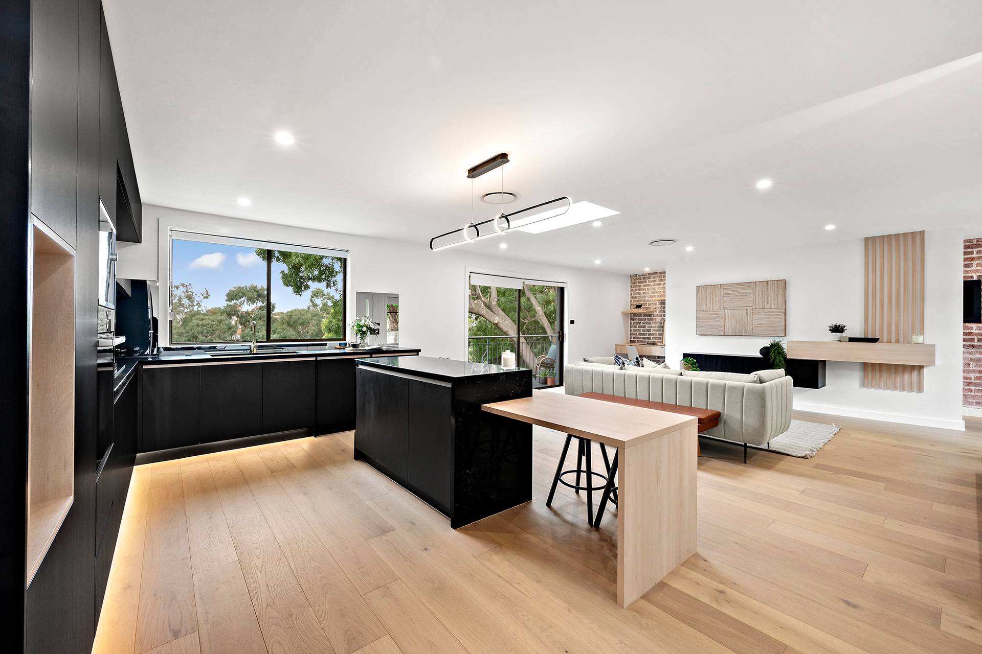 Modern open-plan living room and kitchen with large windows, wood flooring, and sleek black cabinetry.