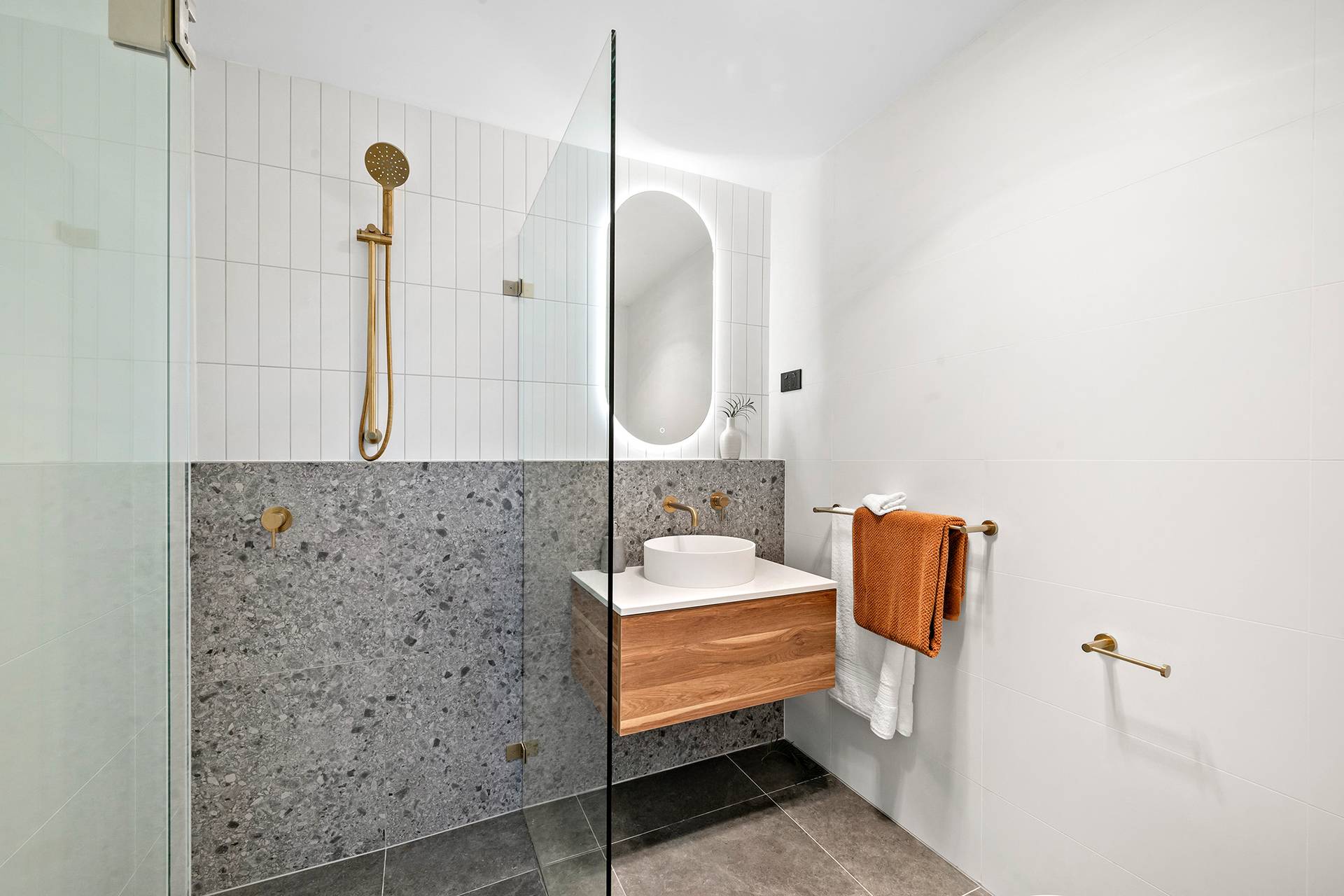 Modern minimalist bathroom with glass shower, wooden vanity, and gold fixtures.
