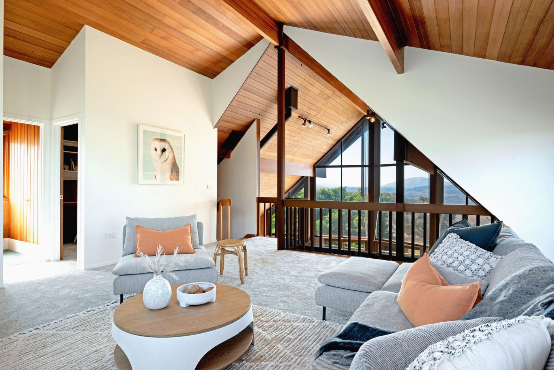 Modern living room with large windows, gray sofa, wooden ceiling, and owl artwork.