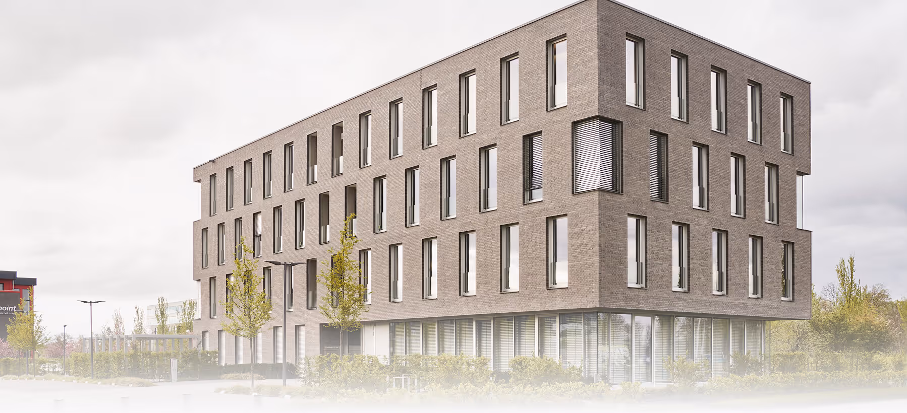 Modern rectangular office building with large windows and small trees outside on cloudy day.