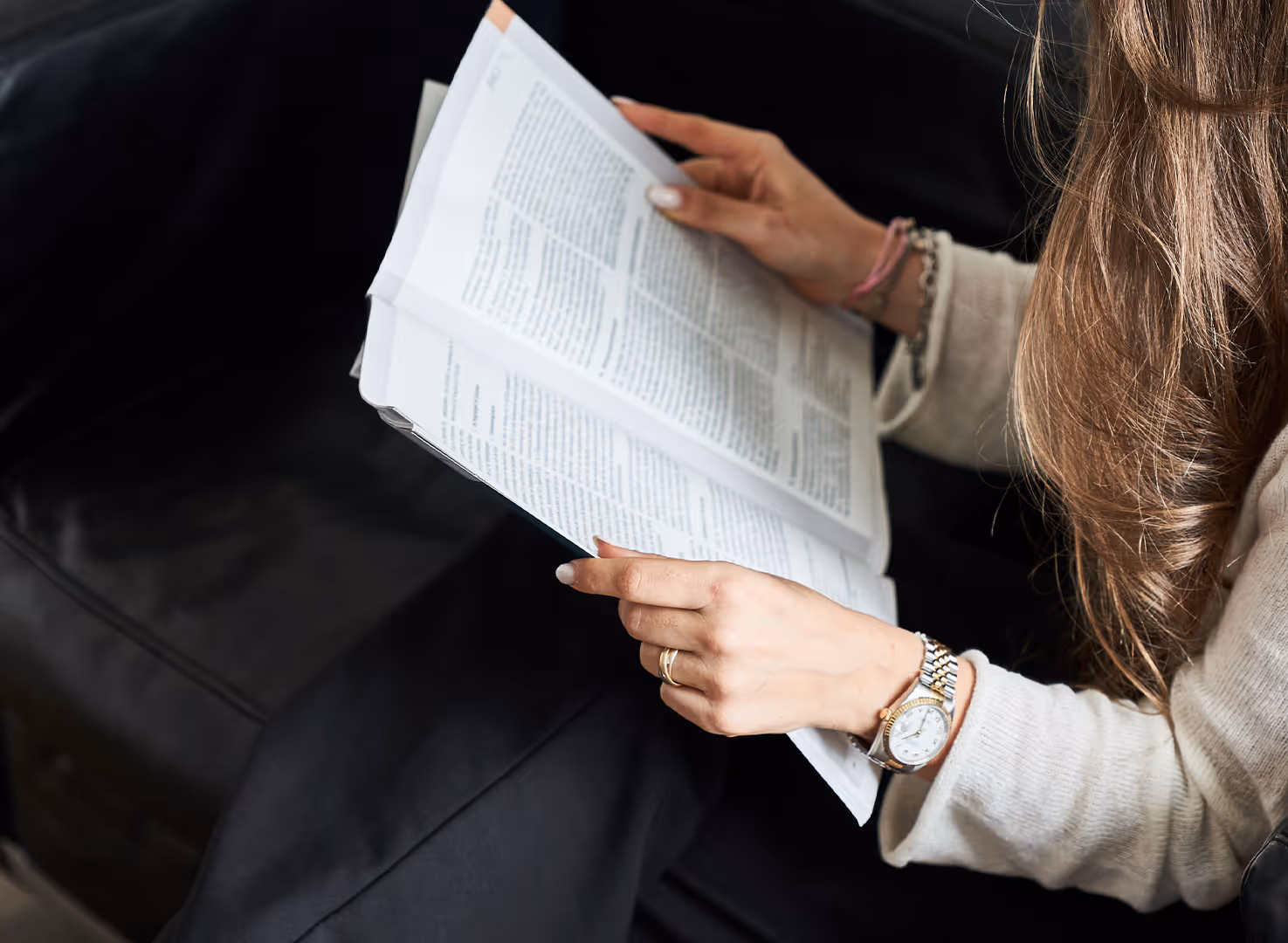 Frau mit langem Haar liest ein aufgeschlagenes Buch auf schwarzem Sofa.