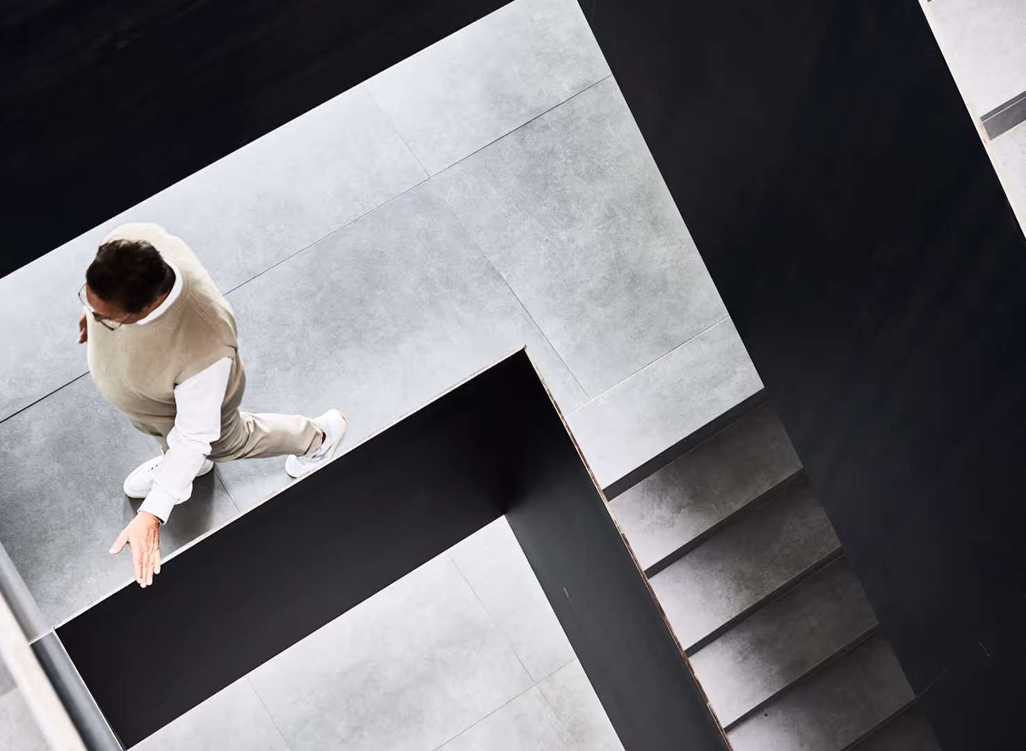 Ein Mann in hellen Kleidern läuft die Treppe einer modernen, minimalistisch gestalteten Treppenhaus.