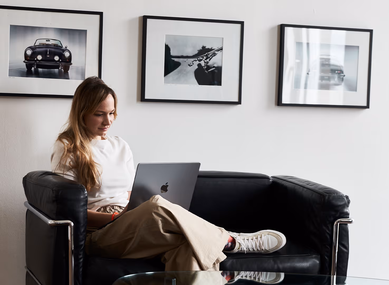 Frau sitzt auf schwarzem Sofa und arbeitet mit Laptop vor weißen Autobildern an der Wand.