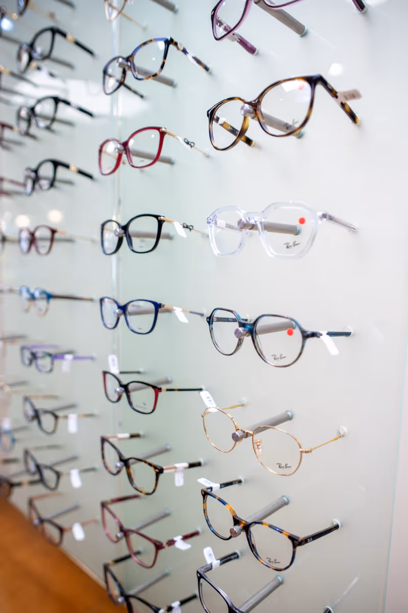 Display of multiple eyeglasses frames in various colors and styles on white wall.
