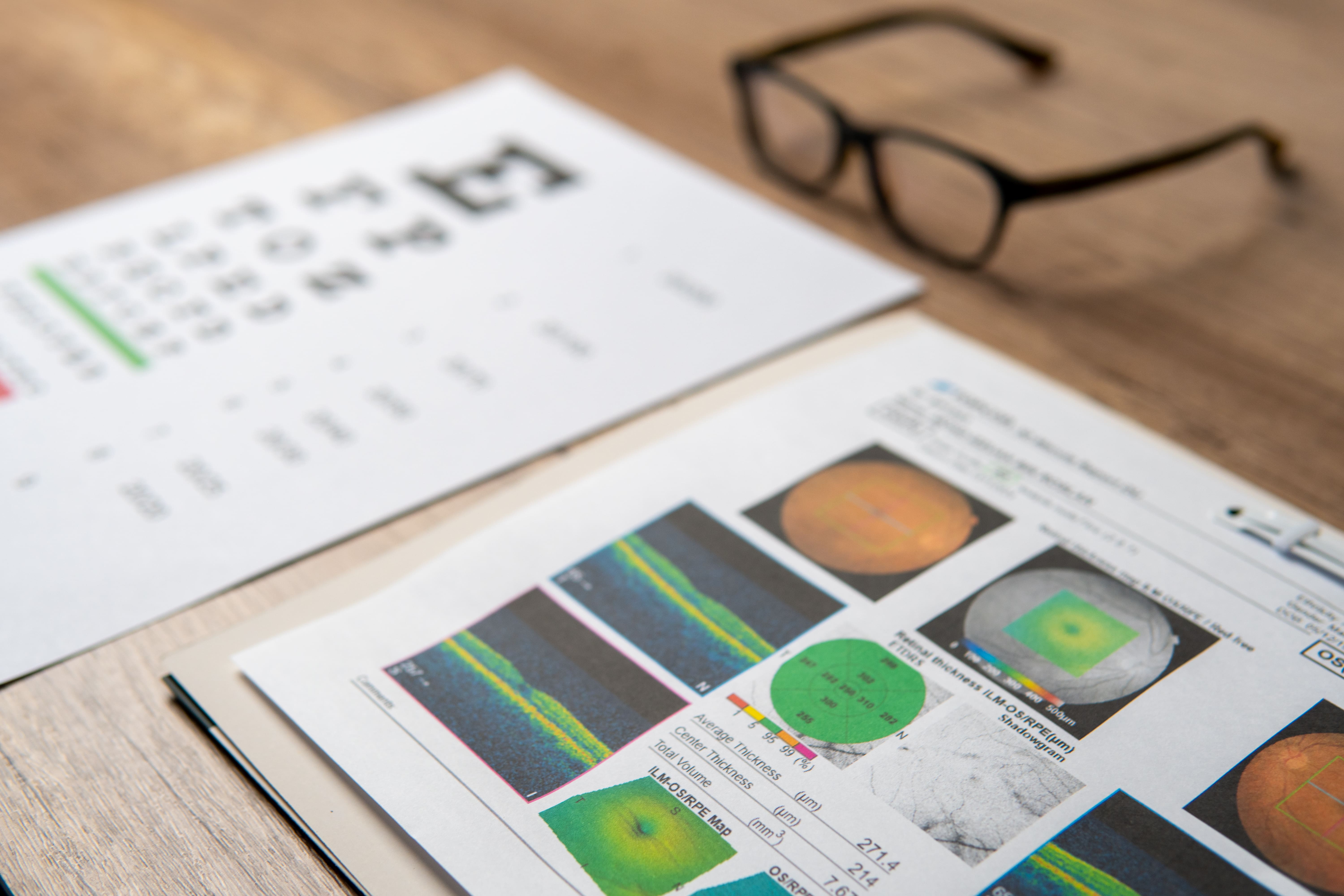 Printed data analysis documents with charts, graphs, and images on wooden desk with glasses.