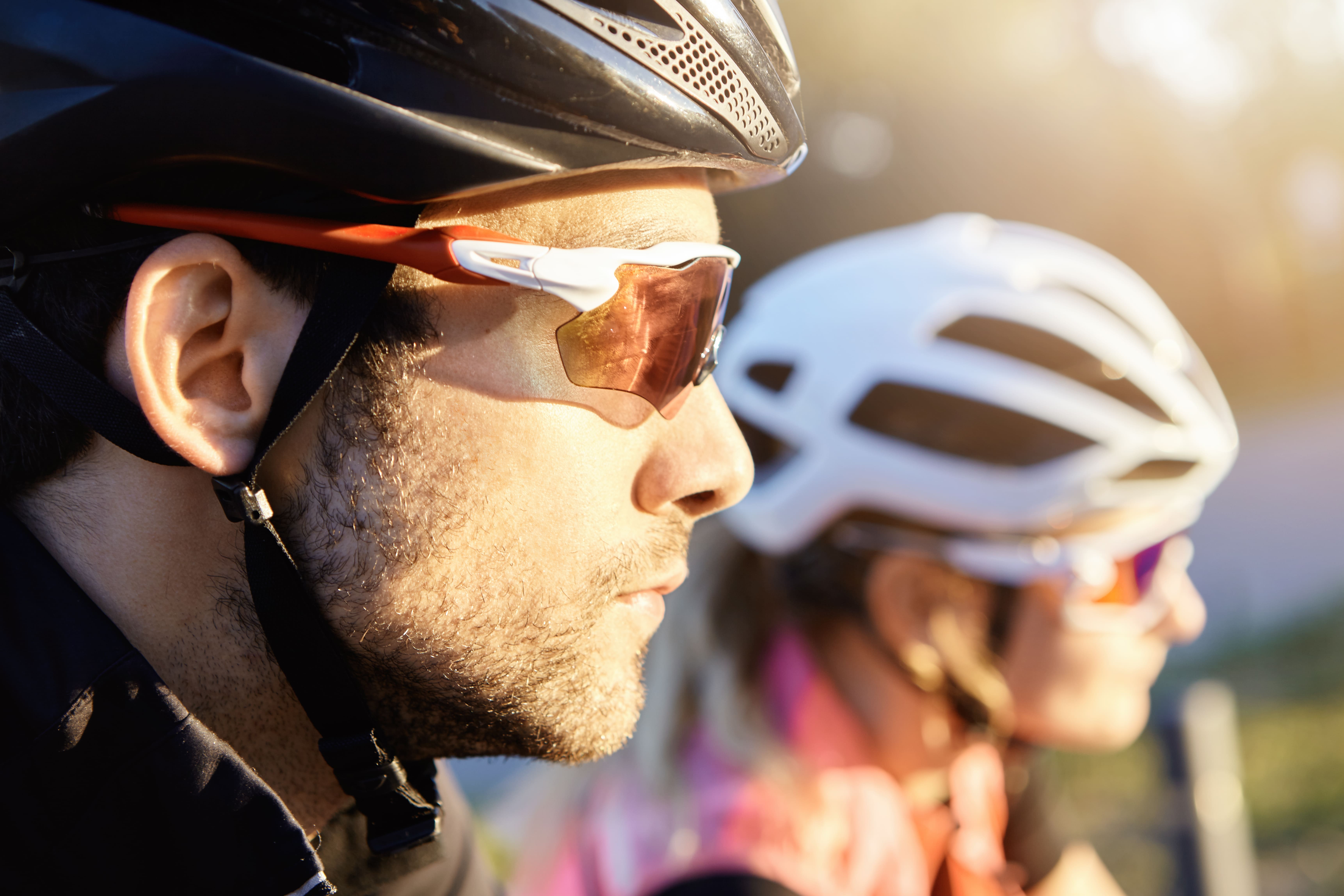 Cyclist wearing black helmet and orange-tinted sunglasses in profile view outdoors