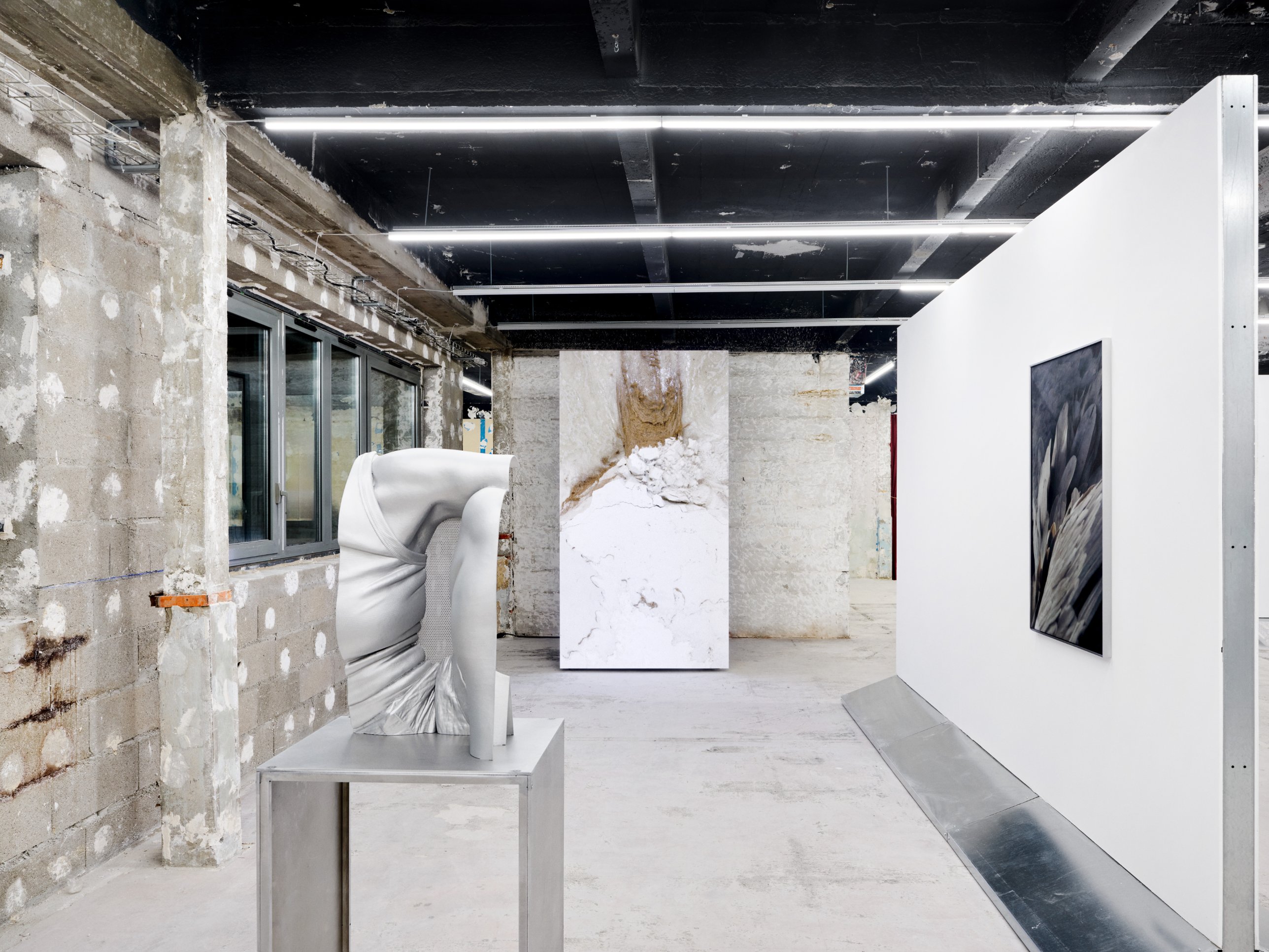 Vertical LED screen showing white mineral textures and sand, framed by a sculpture and a hanging wall