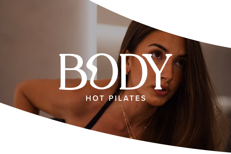Woman with long hair exercising indoors with BODY Hot Pilates logo overlaid.