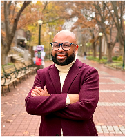 Desmond Upton Patton smiling on campus walkway, promoting joy and resilience through trauma-informed research.