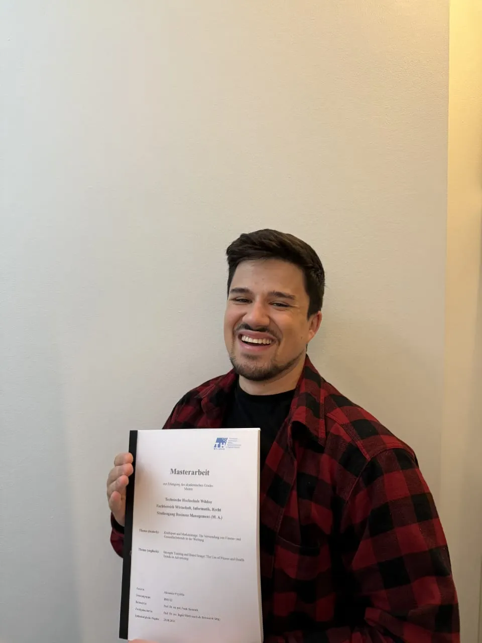 Alex steht mit seinem Master-Abschluss im Marketingmanagement vor einer weißen Wand.