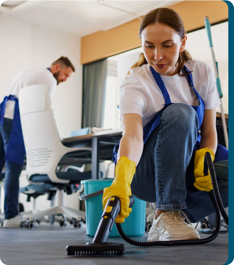 Reinigungskraft mit Handschuhen beim gründlichen Saugen unter einem Schreibtisch in einem modernen Zuhause oder Büro.