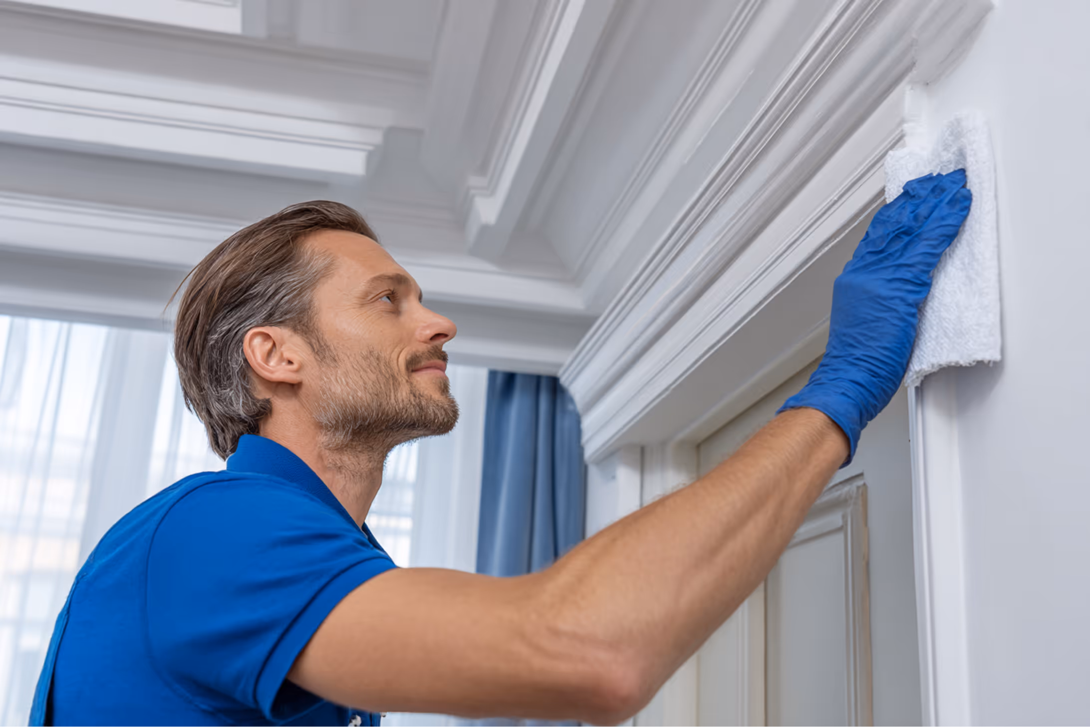 Reinigungskraft wischt mit einem Tuch gründlich Zierleisten oder Deckenverzierungen ab – für ein gepflegtes Zuhause.