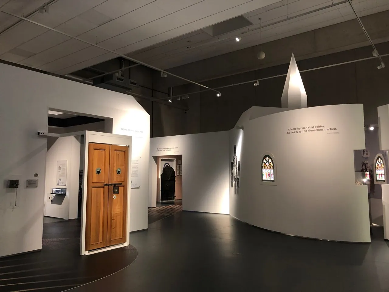 Blick in die Dauerausstellung des Raums, im Vordergrund ist eine römische Tür zu sehen, im Hintergrund eine stilisierte Kapelle. 
