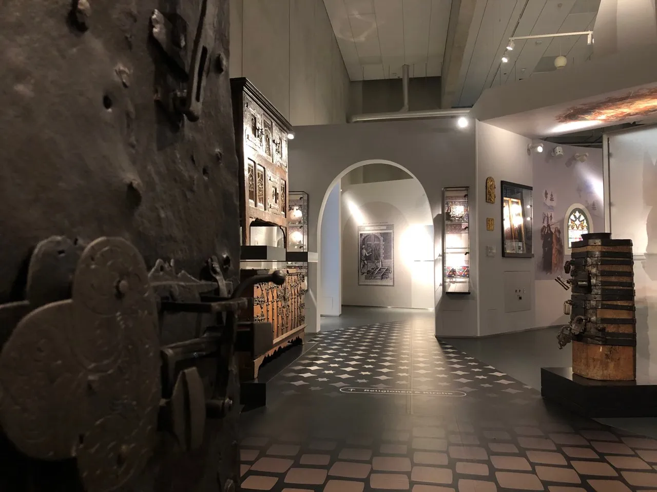 An einer eisernen Tür vorbei richtet sich der Blick in die Dauerausstellung des Museums, wo man unter anderem einen hölzernen Opferstock mit sechs Schlössern sieht. 