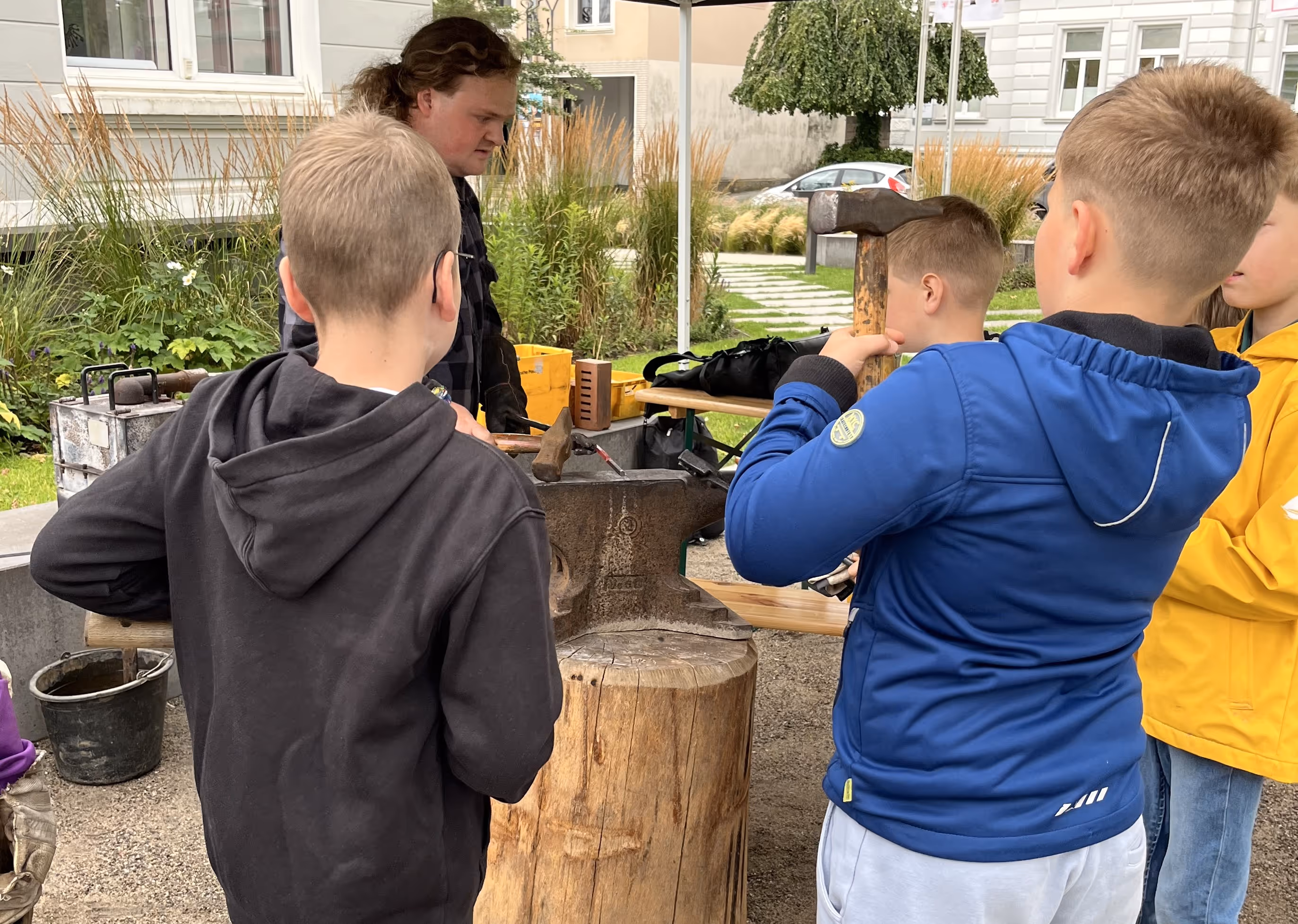 Kinder stehen um einen Amboss herum und schmieden zusammen ein Messer aus Eisen. 