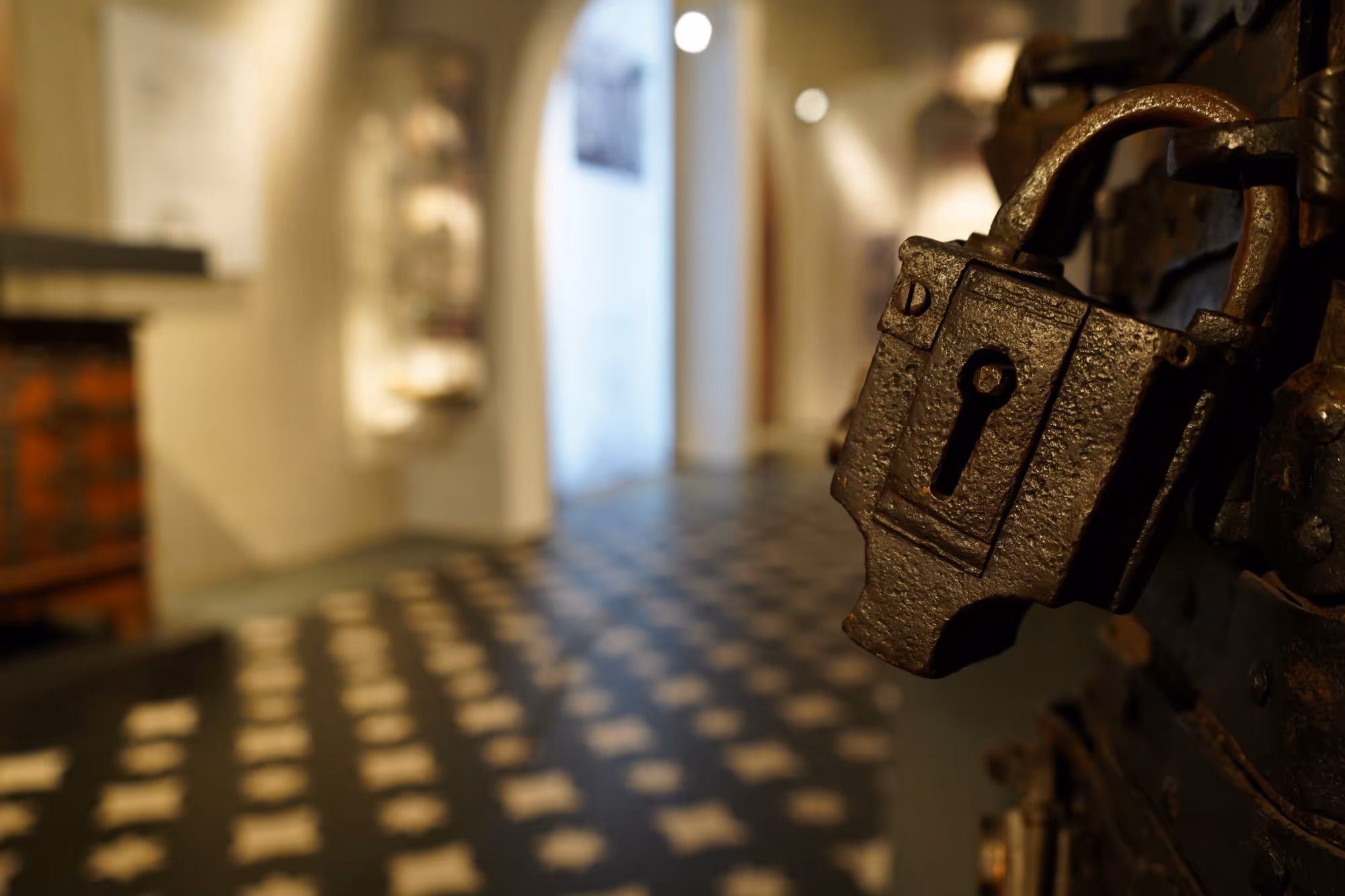 Ein großes eisernes Schloss, das an einem Bügel befestigt ist, ist im Vordergrund, dahinter liegt die Ausstellungshalle mit weiteren Exponaten des Museums.