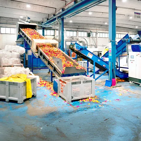 An industrial recycling facility with conveyor belts sorting and moving shredded, colorful plastic pieces into large bins.