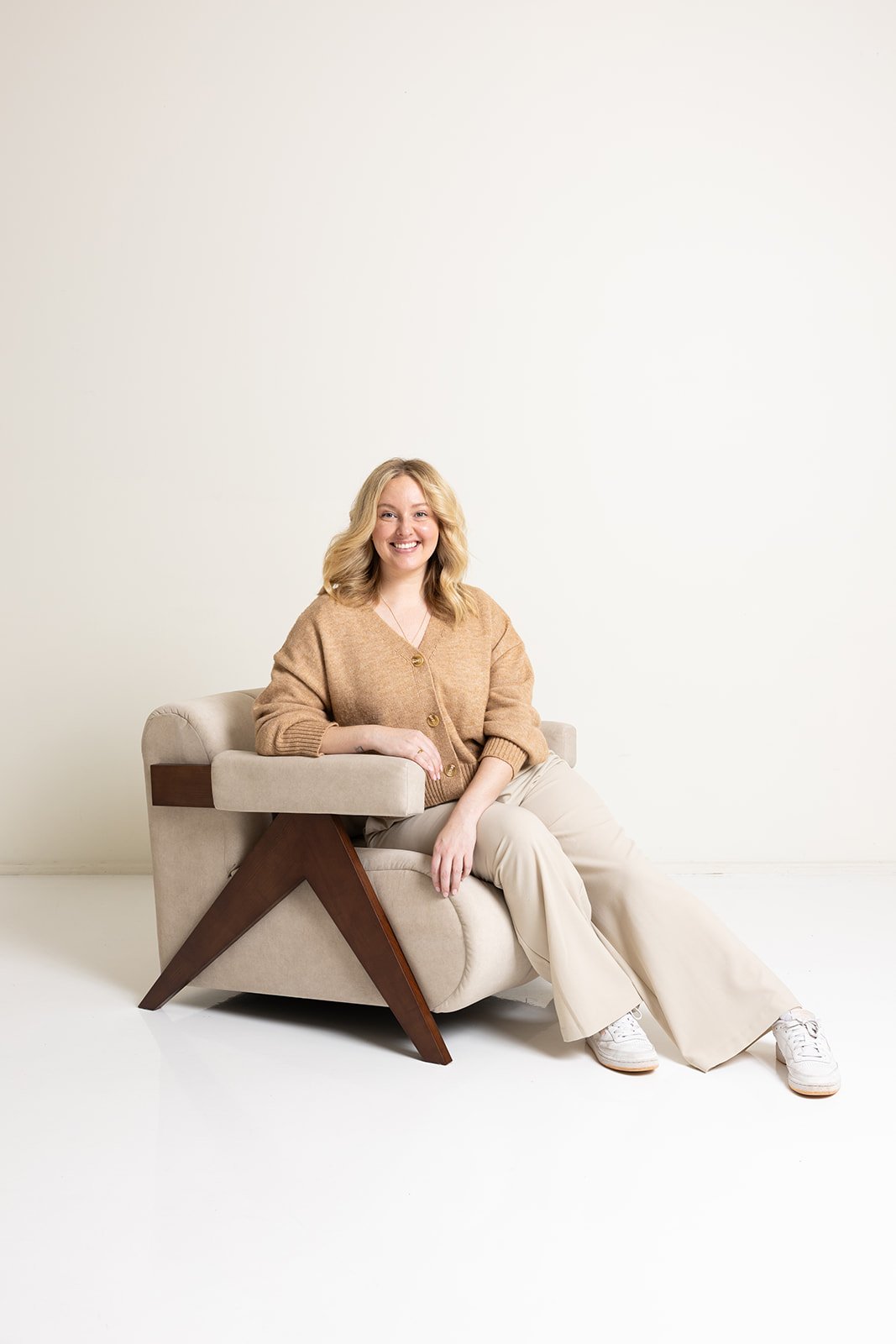 Hayleigh in a beige sweater and pants sitting on a couch