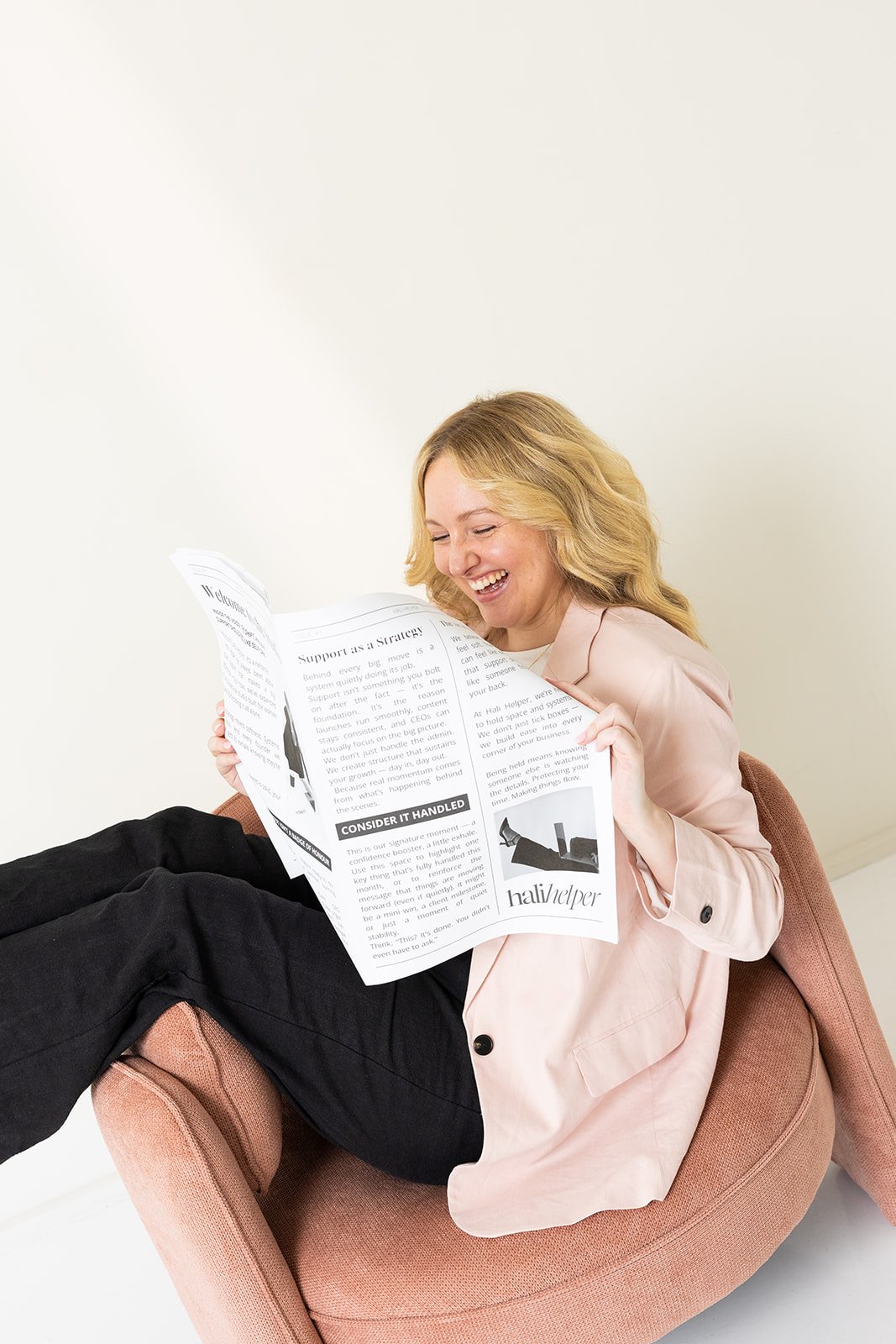 Hayleigh smiling while sitting on a couch and reading a newspaper