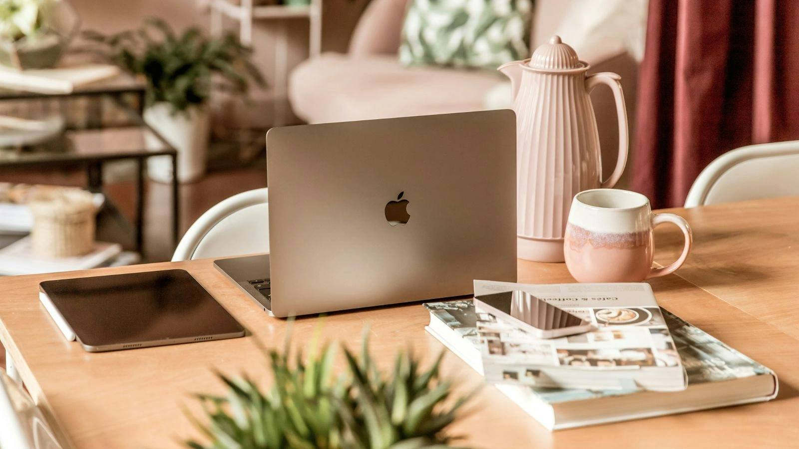 A laptop, two books, an iPad and iPhone, a tea pot and a cup on meeting table