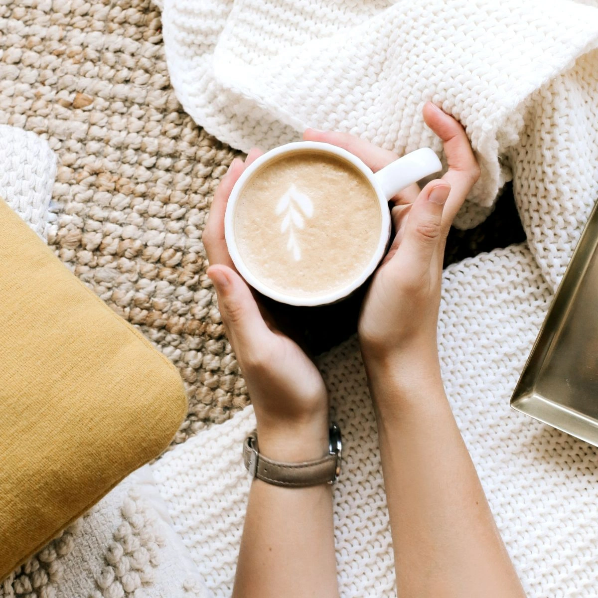 Close-up shot of two hands holding a cup of coffee over white and beige knitted cloths