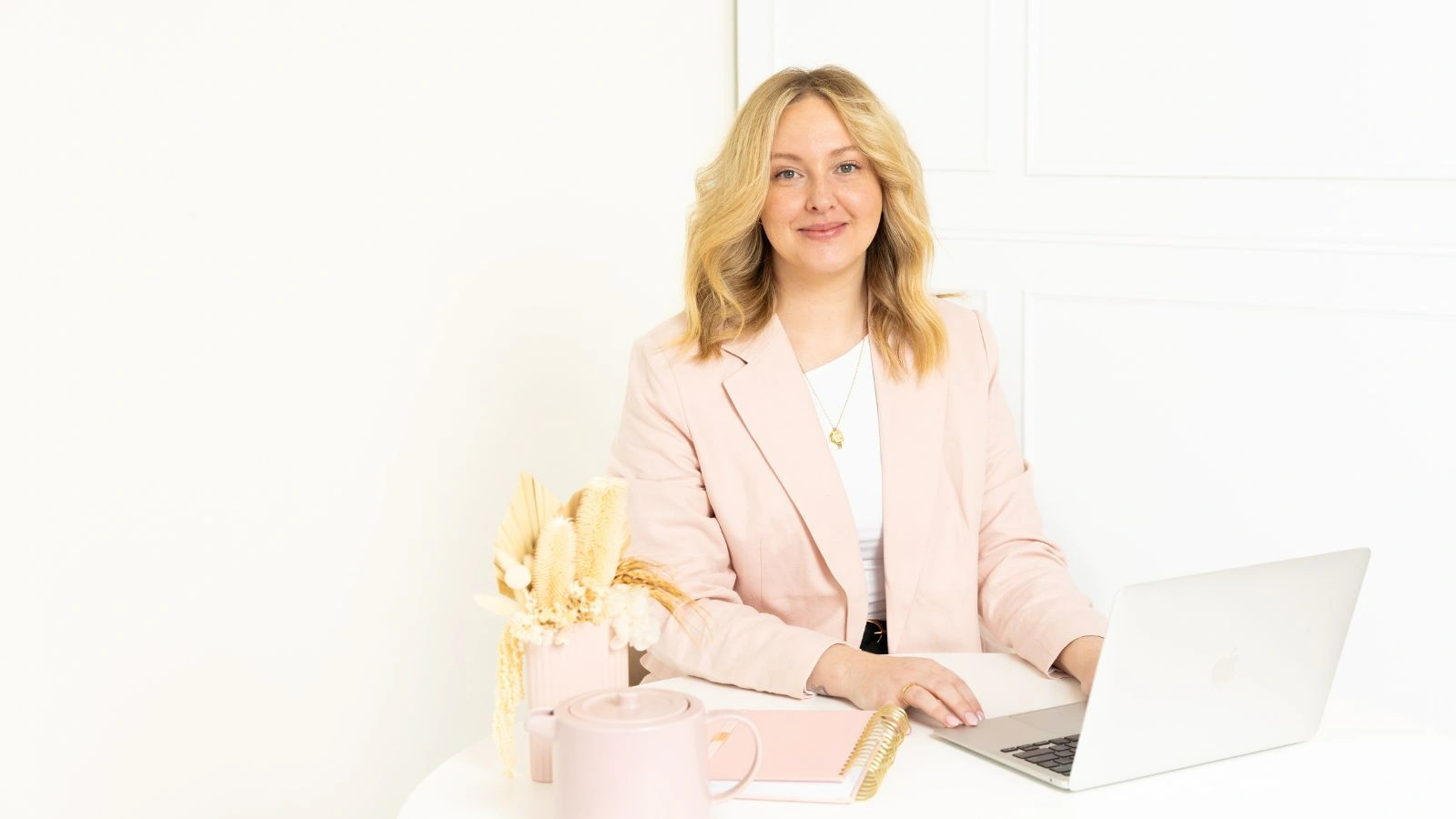Homepage banner featuring Hayleigh Watson, the owner and head of Hali Helper, working on her laptop with a notebook, flowers and a teapot on the side