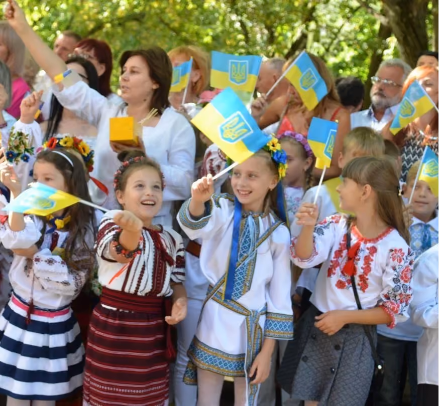 Ukrainische Kinder in Tracht mit Ukraine-Flaggen bei einer Schulfeier