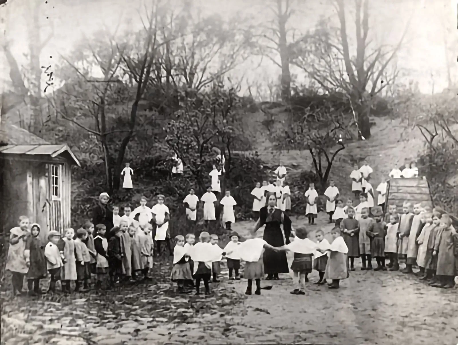 Children and teachers in the yard of the Kinder Farzorgnt (Child Care) orphanage and school at 39 Ostra Brama Street. In the center is teacher Rivka Gordon (Tolpin). (Vilna, 1918).