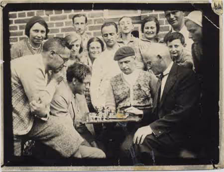 Men playing chess as a crowd looks on at the Kultur Lige (Jewish Workers\' Cultural Association) summer colony (Karvye, Poland, 1928).