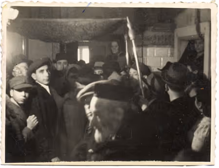 The badkhn (merry-maker) performs at a wedding in the Lublin Ghetto, as guests stand under the he traditional wedding canopy huppah (Lublin, 1942).
