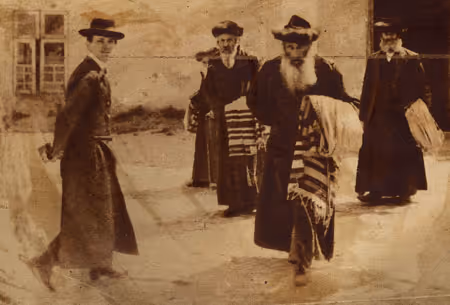 Traditionally dressed men in kapotes (holiday outer garments) and shtraymlen (fur-rimmed hats), carrying taleysim (prayer shawls), leaving the synagogue (Poland, 1932).