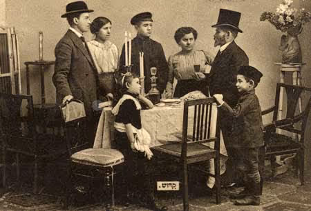 Postcard tableau of a well-to-do family gathered around a festive table for the Kiddush (blessing over the wine) in Poland (circa 1910).