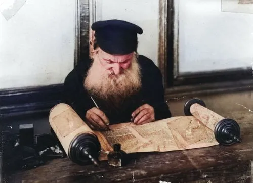 Dovid Elye, a soyfer (scribe), at work with a quill on a Torah scroll. As soyfer, he also was called upon to letter tefillin, mezuzot, and ketubes (wedding certificates). (Rakhev, Ukraine, circa 1912).