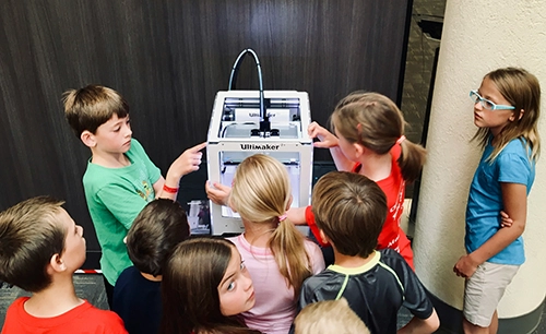 A group of children on a school trip are shown a 3D printer and have to practice their problem solving skill in finding out how to use it. 